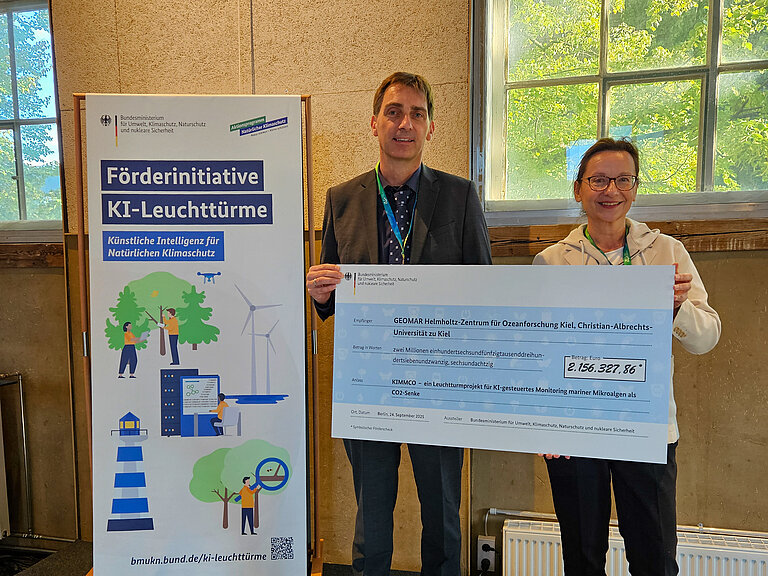 Ein Mann und eine Frau halten einen großen symbolischen Scheck in den Händen