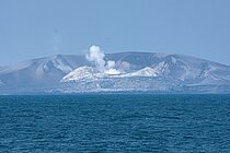 [Translate to English:] Ein rauchender eingestürzter Vulkankegel im Meer