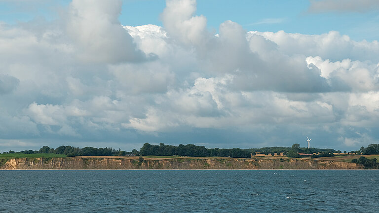 Eine grün bewachsene Steilküste, davor das Meer, darüber ein blauer Himmel mit weißen Wolken