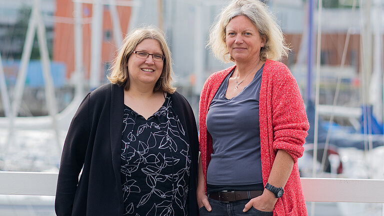 Zwei Frauen stehen auf einem Steg und schauen lächelnd in die Kamera