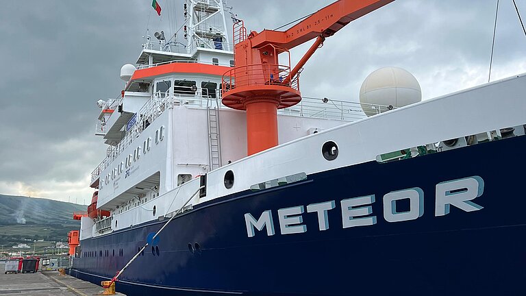 Ein Schiff liegt am Kai, an Deck ist ein orangener Kran zu sehen