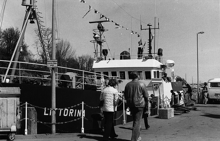 Ein Schwarz-Weiß-Foto von einem Schiff am Kai mit Fußgängern
