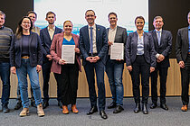 Eine Gruppe Menschen steht vor einer großen Projektionsfläche und schaut in die Kamera