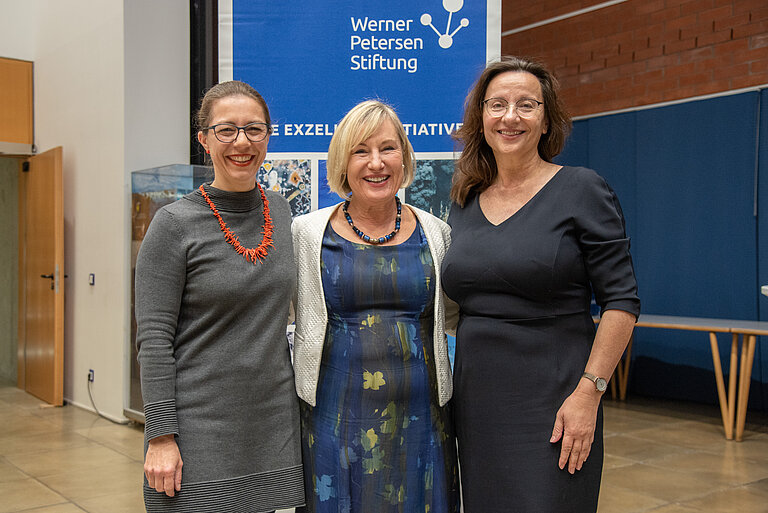 Three women stand arm in arm