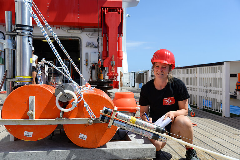 Eine Frau mit Helm hockt an Bord eines Schiffes neben wissenschaftlichen Messgeräten