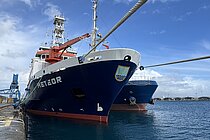 Ein Schiff ist mit Seilen an der Hafenmauer festgemacht. Der Himmel ist blau. 