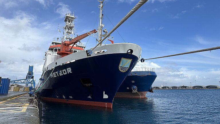 Ein Schiff ist mit Seilen an der Hafenmauer festgemacht. Der Himmel ist blau. 