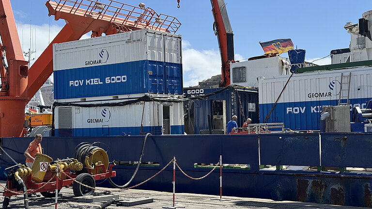 Container werden mit einem Kran an Bord eines Schiffes im Hafen gehievt.