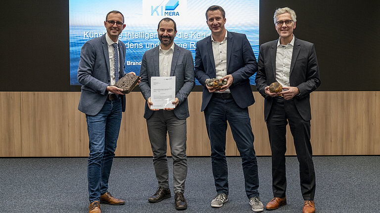 Vier Männer stehen vor einer Leinwand in einem Konferenzraum