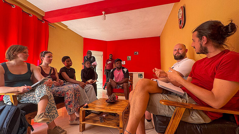 Einige junge Menschen sitzen mit einem älteren Mann um einen niedrigen Tisch