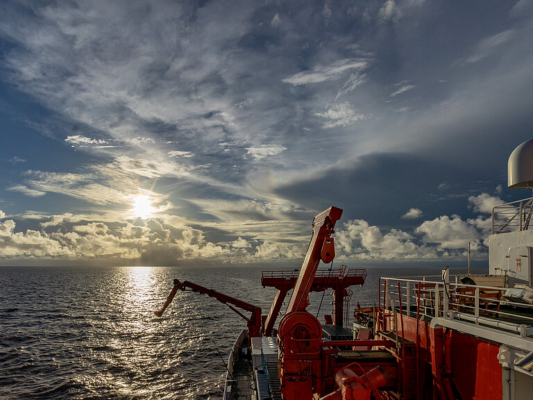 Die Sonne geht über dem Meer auf, im Vordergrund ist der Bug eines Forschungsschiffes zu sehen.
