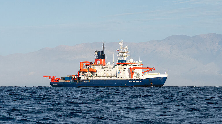 Forschungsschiff auf dem Meer, im Hintergrund die Küste einer Insel
