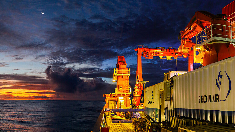 Ein Forschungsschiff mit Containern an Bord im Sonnenuntergang auf dem Meer