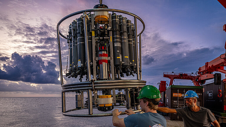 Ein Mann mit einem grünen Helm bringt ein wissenschaftliches Gerät vom Schiff ins Wasser