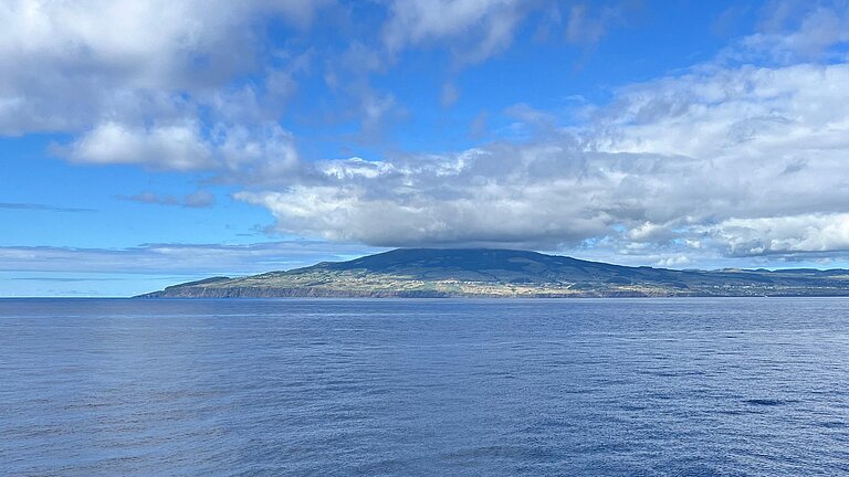Eine Insel im Meer, das Meer ist sehr blau und der Himmel auch