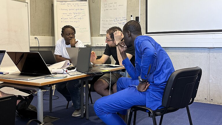 Three young people of different skin colours sit at a desk and discuss