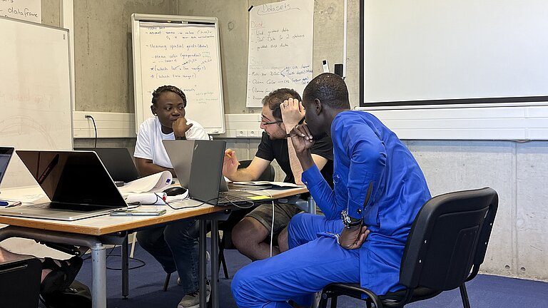 Drei junge Menschen verschiedener Hautfarben sitzen an einem Schreibtisch und diskutieren