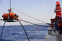 Ein OBEM mit orangenen Auftriebskörpern hängt am Kran des Forschungsschiff SONNE. Foto: Thore Sager/GEOMAR