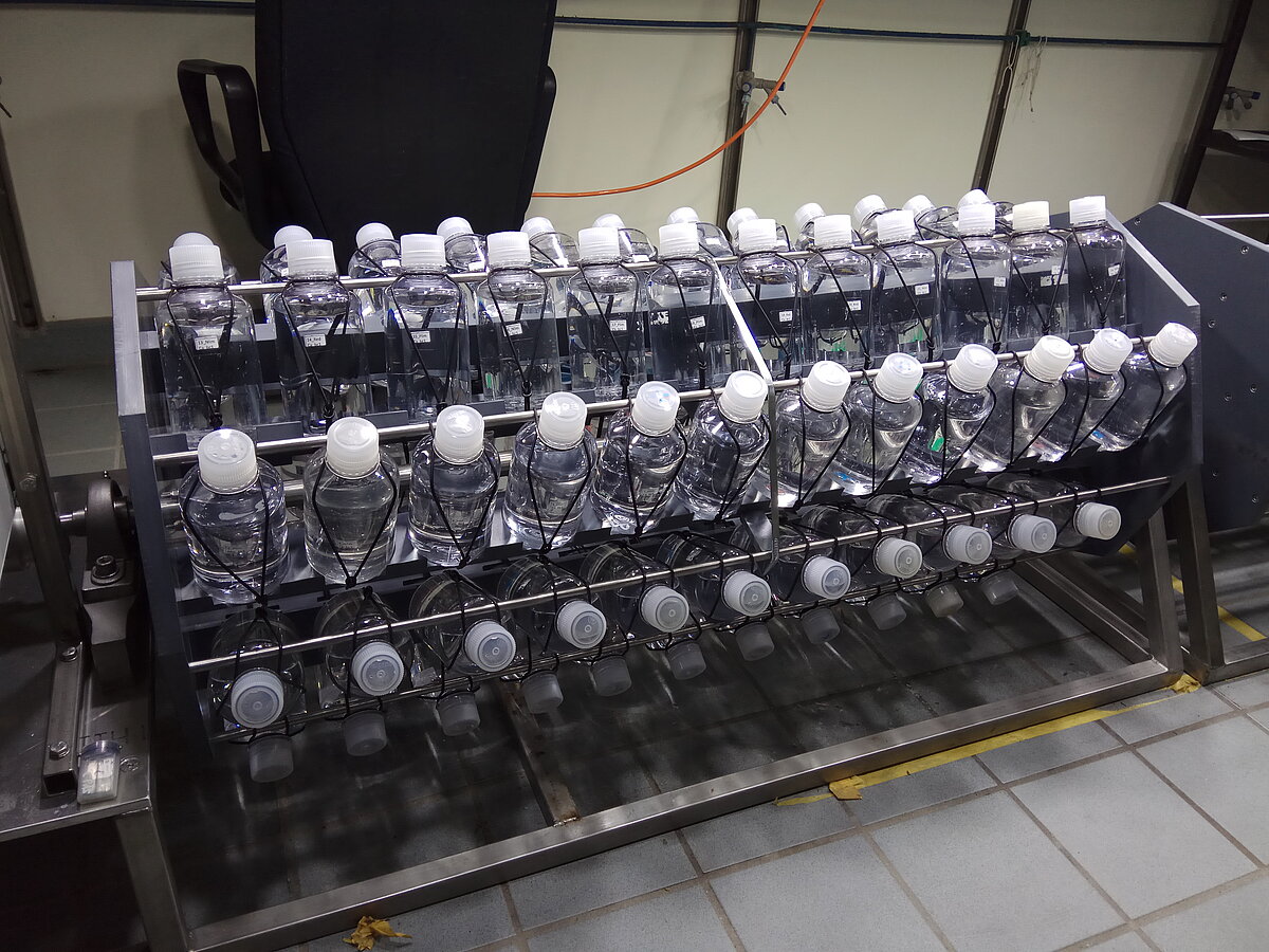 Viele Kunststoffflaschen mit Seewasserkulturen sind an einer Walze befestigt, die sich drehen kann.