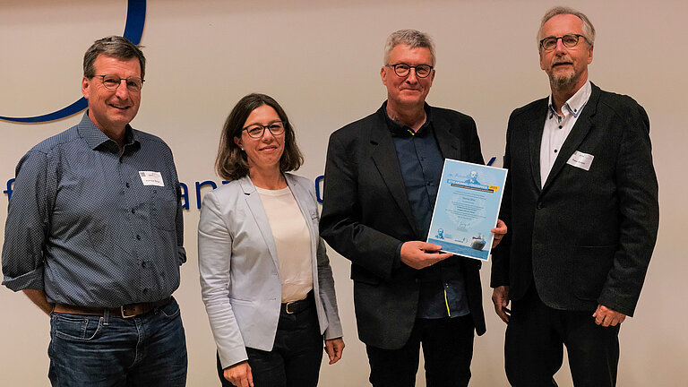 Drei Männer und eine Frau mit einer Urkunde