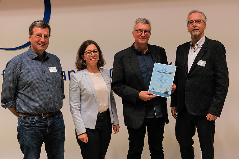 Three men and a woman with a certificate