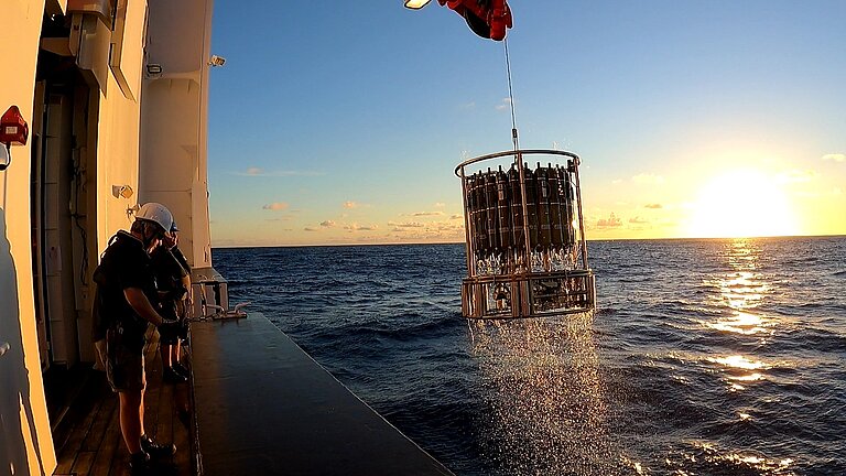 Ein Kranzwasserschöpfer wird bei Sonnenuntergang an Bord eines Forschungsschiffes gehievt
