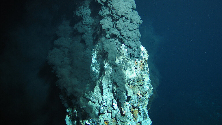Schwarzer Rauch quillt aus einer Fels-Stele unter Wasser