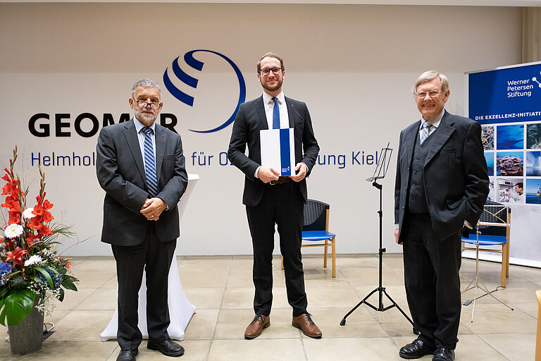 Preisübergabe mit drei Personen im GEOMAR-Hörsaal. 