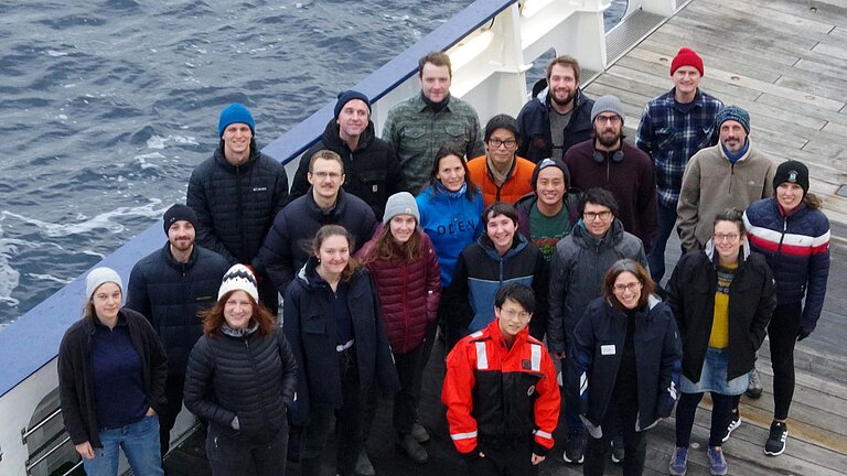 Eine Gruppe Menschen in Winterkleidung an Deck eines Schiffes