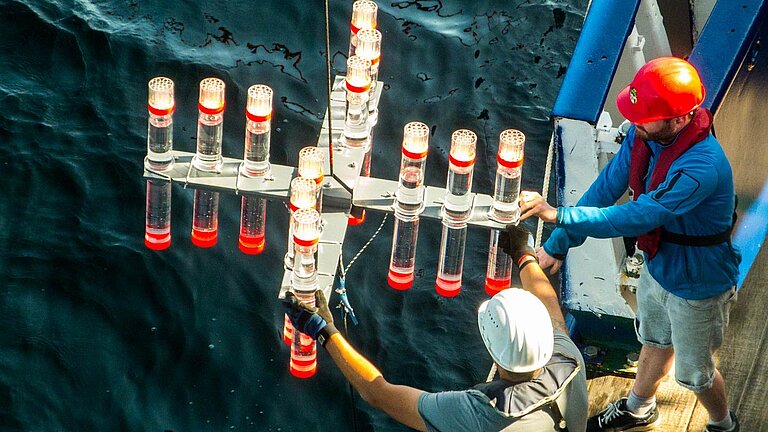Zwei Männer lassen ein Forschungsgerät von Bord eines Schiffes zu Wasser