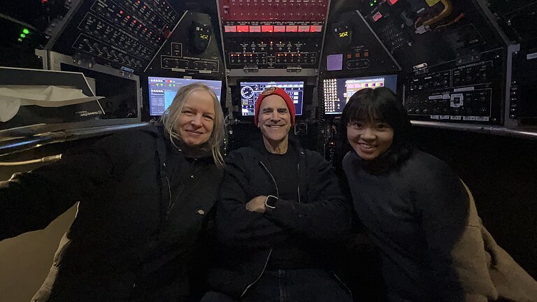 Drei Personen sitzen im Tauchboot ALVIN. Um sie herum Schaltknöpfe und Displays. Sie lachen in die Kamera.