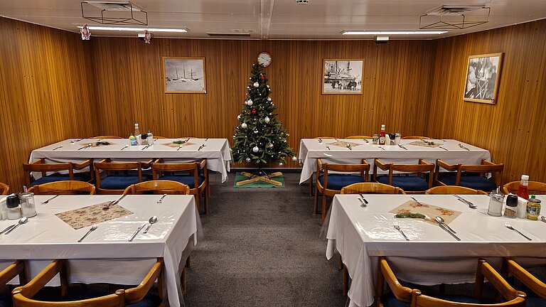 Ein geschmückter Tannenbaum und vier gedeckte Tische in der niedrigen Messe an Bord eines Schiffes