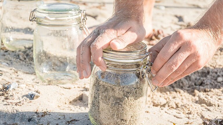Zur Erfassung der Mikroplastikmenge werden Sedimentproben am Spülsaum genommen und in Glasbehälter verfrachtet. 