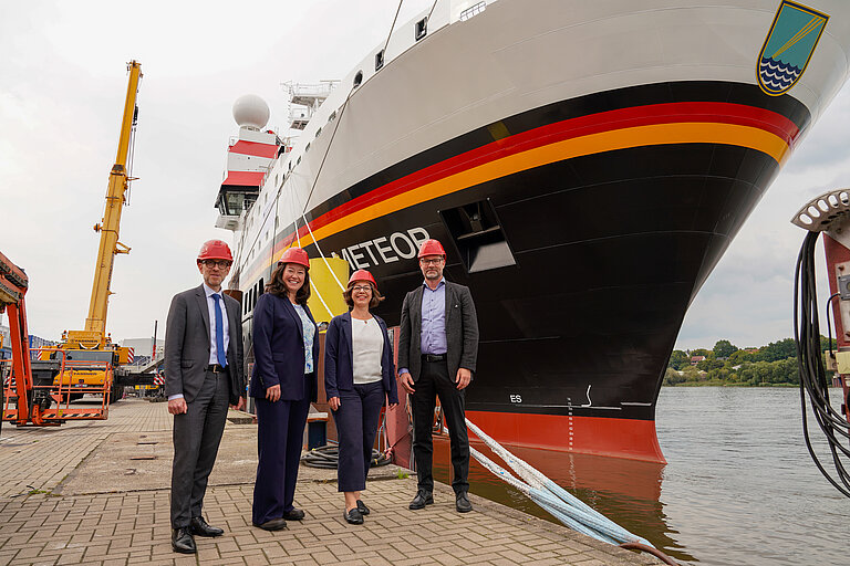 Four people in front of a big ship in a harbour