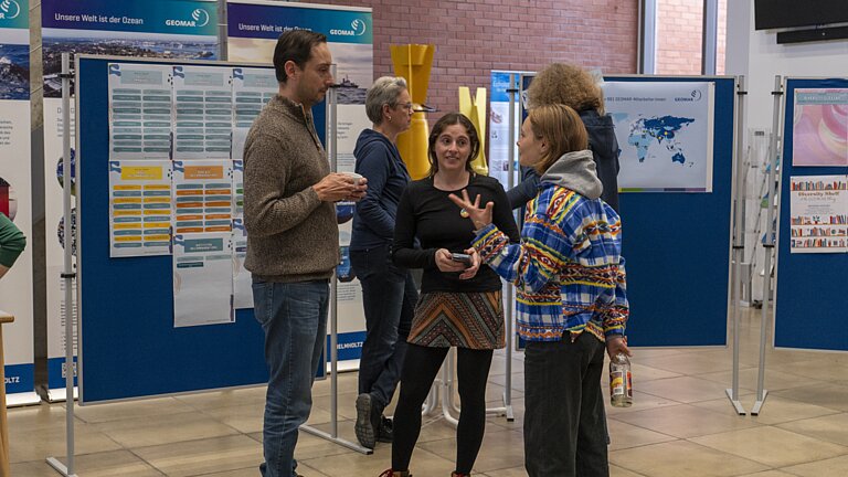 Fünf Personen stehen vor Posterwänden und unterhalten sich