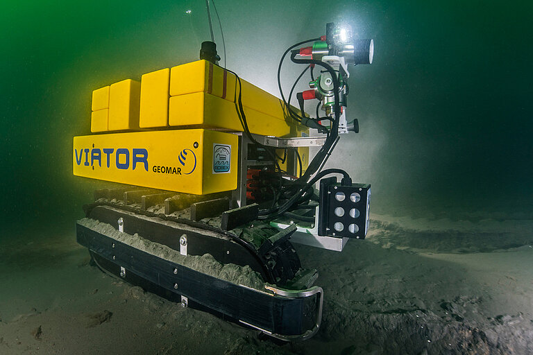 Gelbes quaderförmiges Unterwasserfahrzeug mit Ketten zur Fortbewegung. Es trägt den Schriftzug VIATOR.