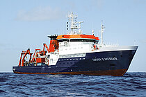 Ein Forschungsschiff mit dunkelblauem Rumpf und weißen Aufbauten auf dem Meer