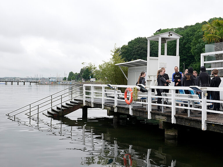 Schüler:innen legen am Steg der Seebar Taucherbrille, Schnorchel und Flossen an.