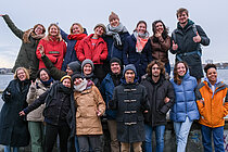 Eine Gruppe Jugendlicher steht auf der Promenade und winkt fröhlich.