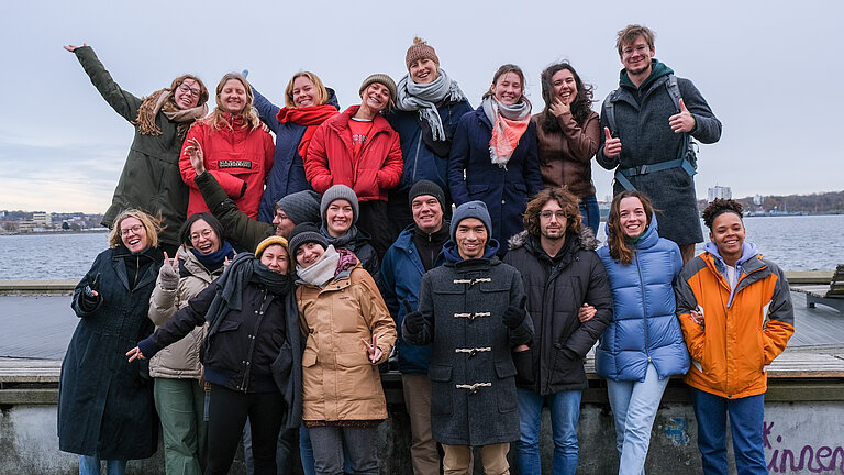 Eine Gruppe Jugendlicher steht auf der Promenade und winkt fröhlich.
