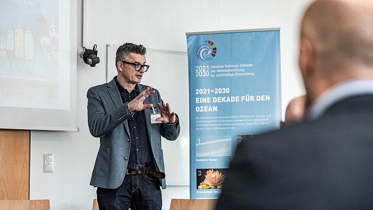 Ein Mann steht vor einem blauen Banner und spricht