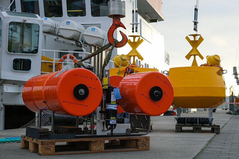 Orange and yellow devices standing on a pier in front of the research vessel ALKOR