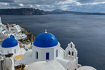 Weiß gekalkte Häuser mit leuchtend blauen Kuppeldächern am Rand einer steil abfallenden Küste