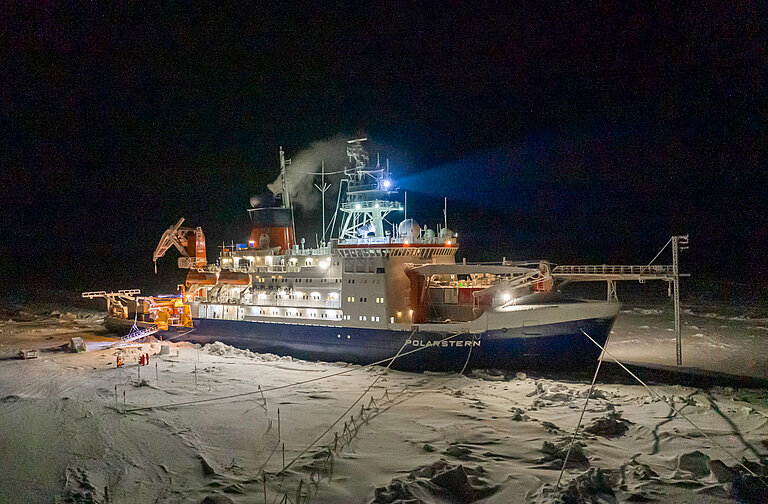 Ein beleuchtetes Forschungsschiff im Eis in dunkler Nacht