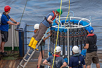 Forschende an Bord eines Schiffes richten den Kranzwasserschöpfer für die Probennahme ein.