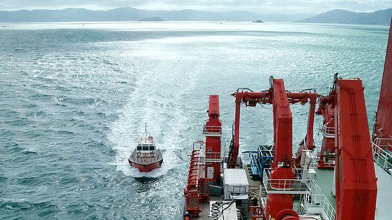 Ein großes rotes Forschungsschiff und ein kleineres Boot auf dem glitzernden Meer
