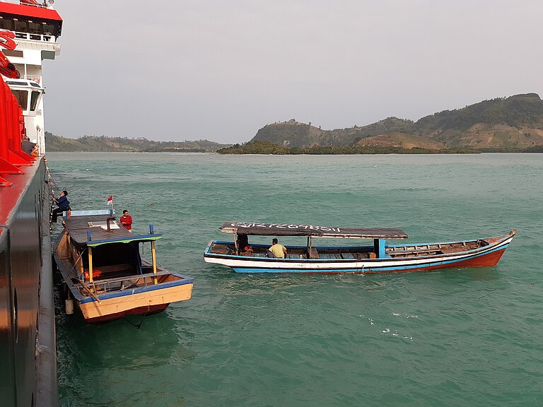 Two wooden boats near the shore mooring to a large research vessel
