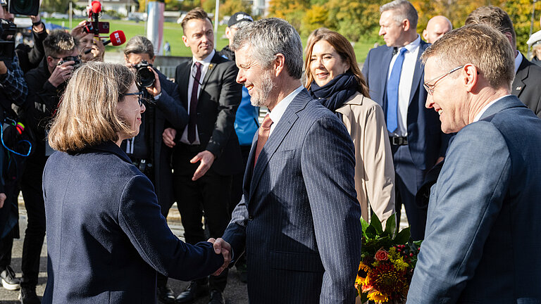 A woman in a dark blue suit shakes hands with a gentleman in a blue pinstripe suit