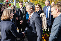 A woman in a dark blue suit shakes hands with a gentleman in a blue pinstripe suit