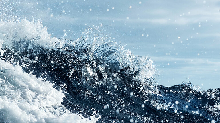 Durch das Speigatt eines Schiffes blickt man auf Wellen, Gischt und Himmel